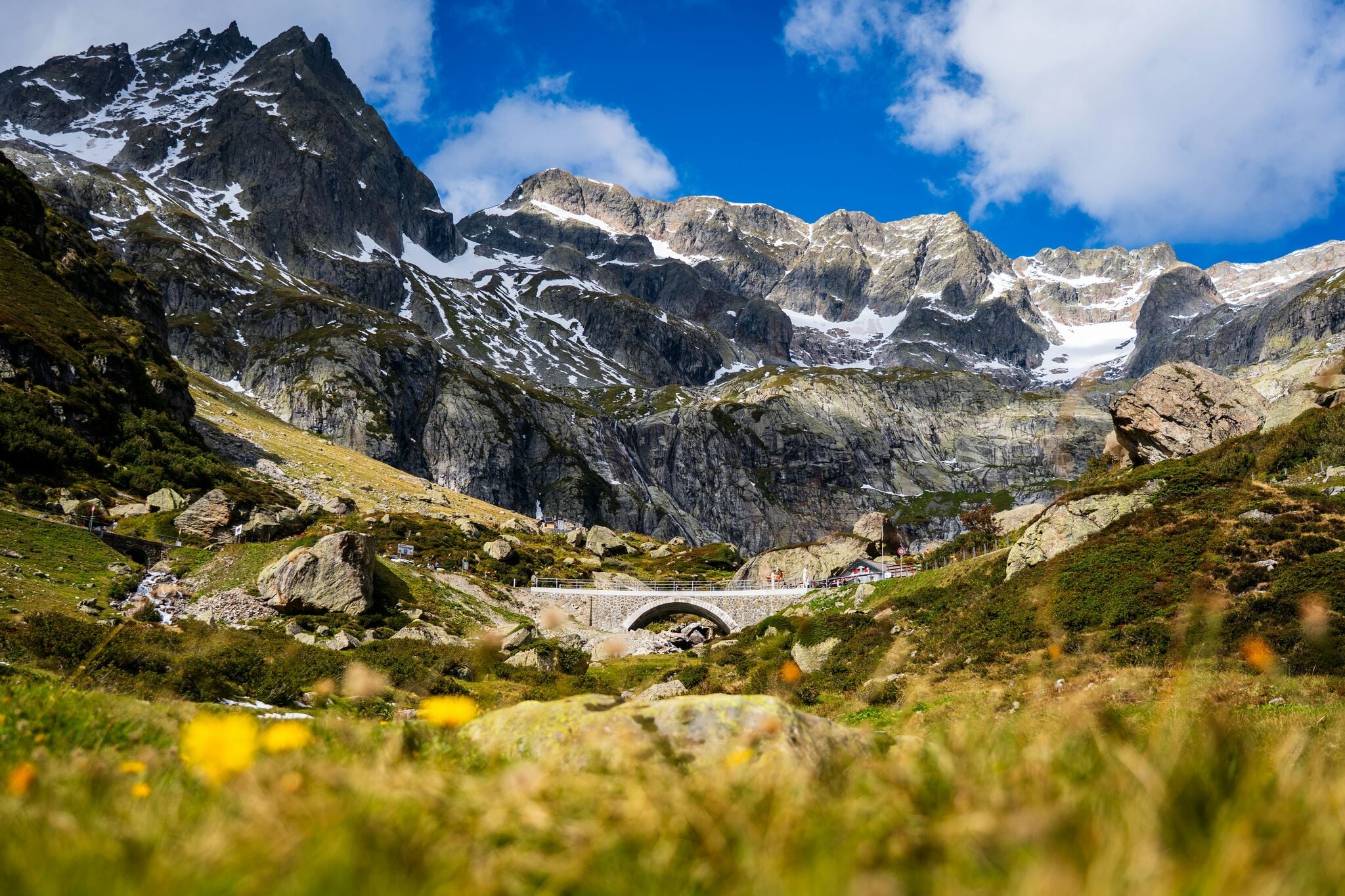 Mountain bridge in snowy alpine landscape with house, combining nature and architecture with scenic rocks and vegetation in daylight.